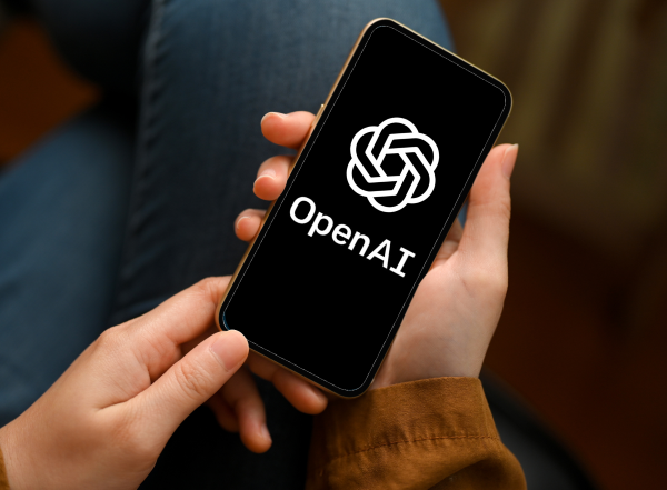 Hands holding a smartphone with the OpenAI logo on the screen.