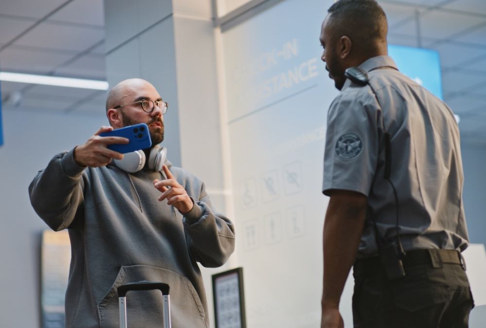 Airport security speaking to male traveler about his cell phone.