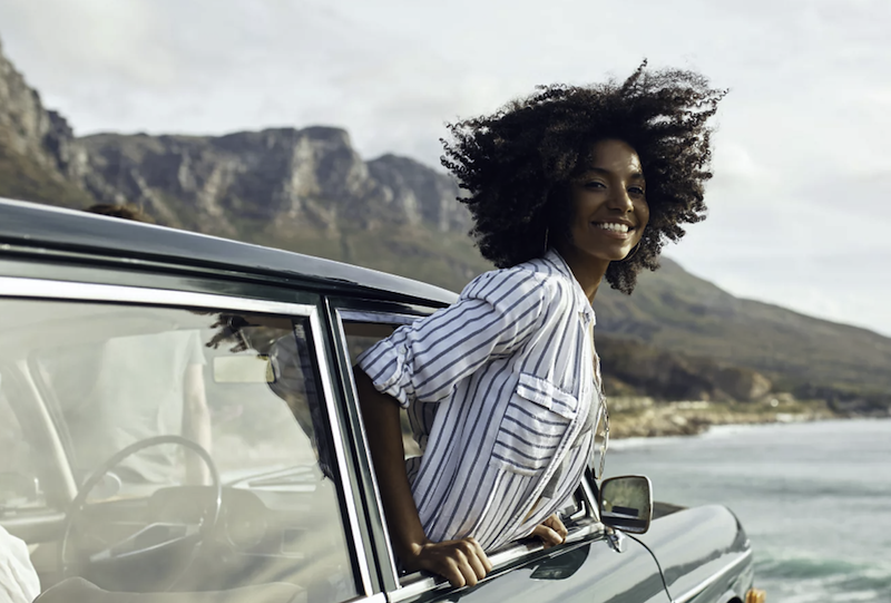 A woman traveling by car A woman sticking her head out of the window while on a road trip.