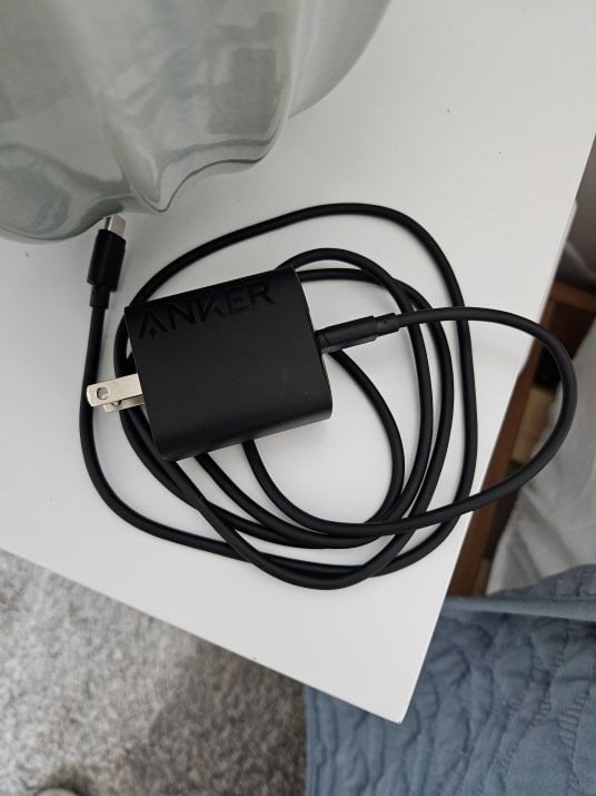 Black Anker USB-C wall charger with its cable coiled on a white table