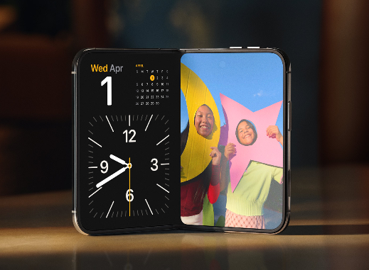 iPhone Duo propped open on a table in StandBy mode, with a clock and calendar on one display and photos on the other.